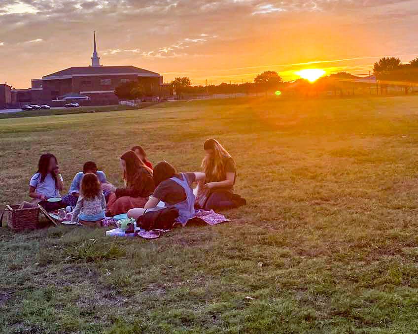 Children sitting and socializing in a field at a homeschool park meetup in Fort Worth Texas.
